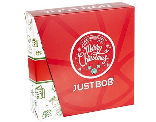 Caja de Justbob XMAS KIT en rojo y blanco con el mensaje 'Te deseamos una Feliz Navidad' y el logotipo de la hoja de cannabis, mostrando un empaque festivo para regalos de weed CBD