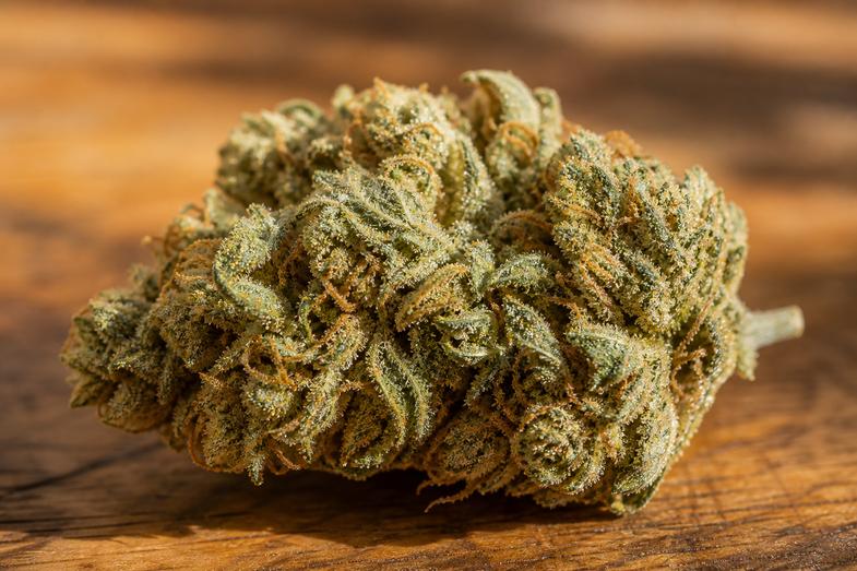 Macro de un cogollo de flor de cáñamo CBD con tricomas resinosos y pistilos anaranjados sobre una superficie de madera, en alusión al perfil cannabinoide