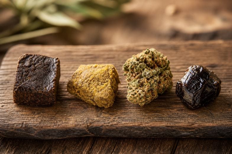 hachis-cbd-variantes-hash-polen-moonrock-charas Cuatro variantes de hachís de cáñamo CBD sobre una mesa de madera: hash clásico, polen prensado, moonrock y charas, en alusión a los formatos del catálogo