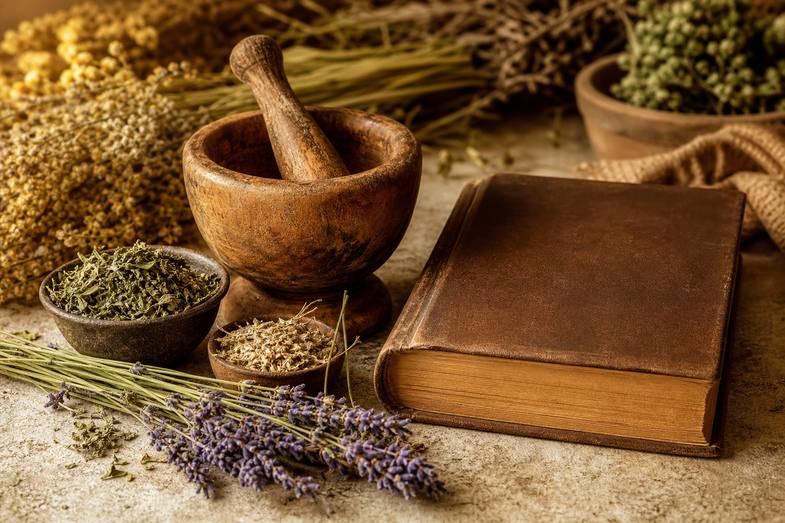 Hierbas secas, mortero de madera y un libro de cuero cerrado junto a ramitas de lavanda en un bodegón de herboristería tradicional